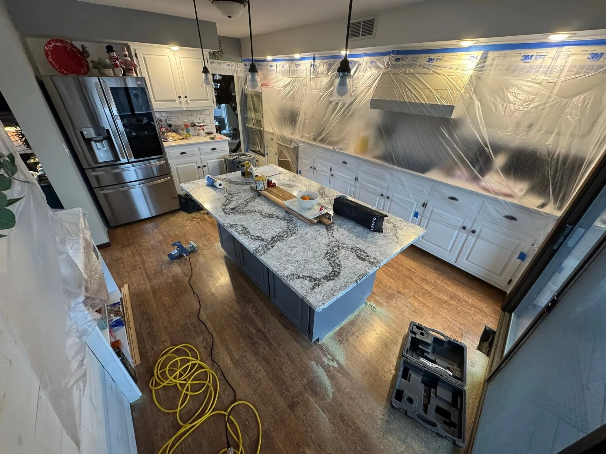 Kitchen island and white cabinets with dark plank flooring after installation, protective sheeting still on the counters